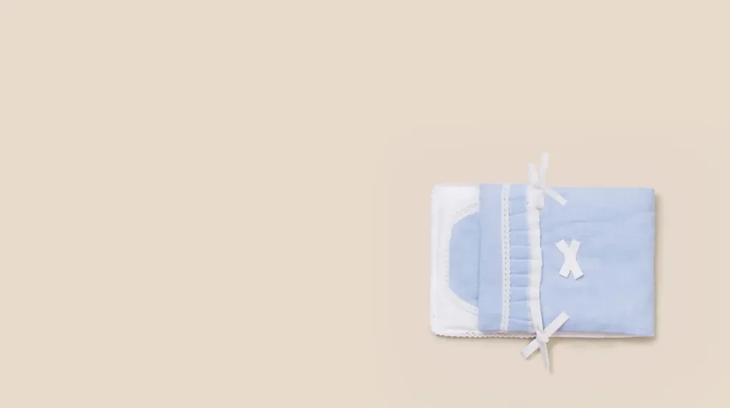 하늘색 면 수의보가 흰 리본 두 개로 묶인 채 베이지 바탕 한쪽에 놓인 모습