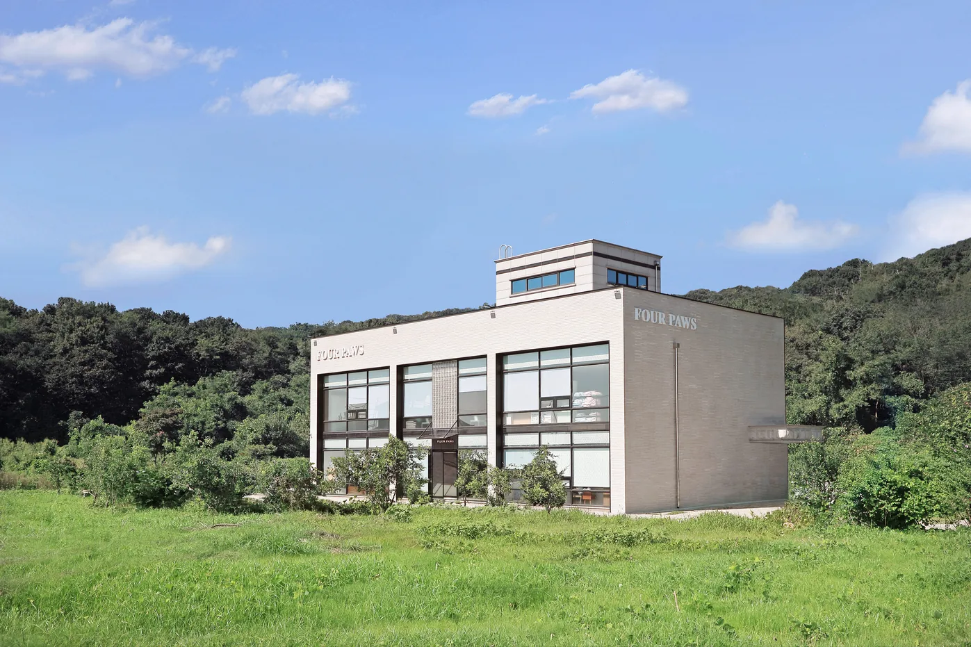푸른 풀밭과 숲을 등지고 선 흰 벽돌 2층 건물, 모서리에 FOUR PAWS 글자가 붙은 화성 2호점