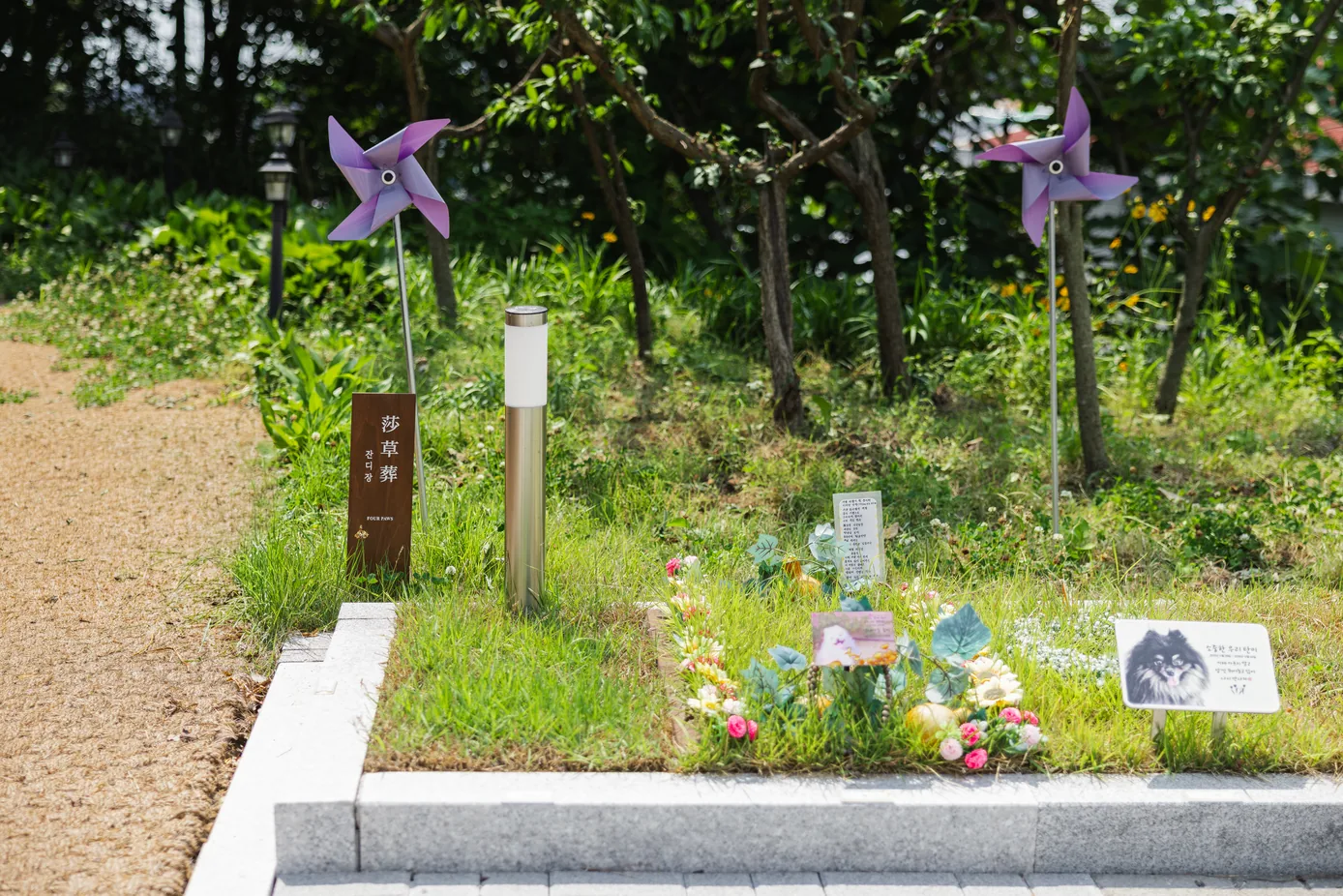 보라색 바람개비와 잔디장 나무 팻말 사이로 조화와 아이 사진 이름표가 놓인 화성 1호점 잔디장