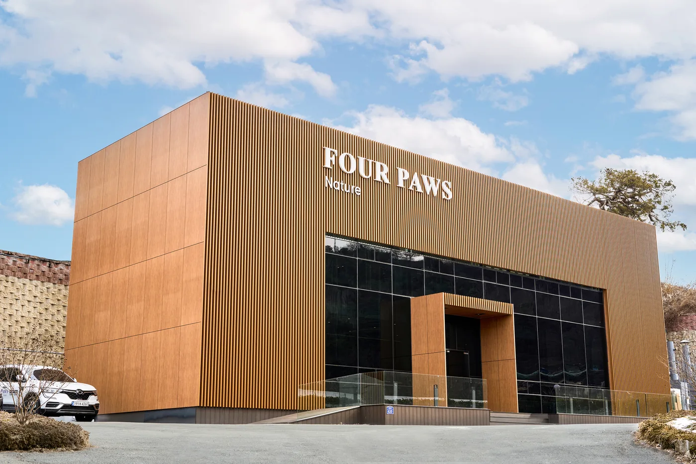 나무 결 외벽에 FOUR PAWS Nature 간판이 붙은 포포즈 세종점 건물과 앞마당에 세워 둔 흰 차
